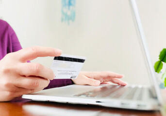 Image of a laptop and someone's hand holding a credit card/debit card