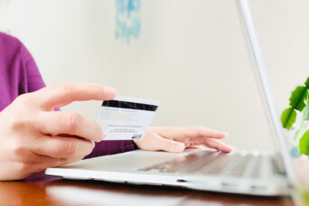 Image of a laptop and someone's hand holding a credit card/debit card