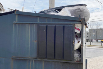 A black dumpster stuffed with trash