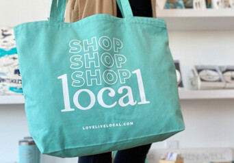 A teal LLL tote bag held by someone in a shop