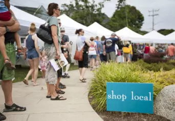 An outdoor festival with white tents, people shopping, and a teal sign that says "shop local"