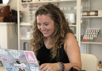 A woman with brown hair in a black shirt working on a laptop and smiling